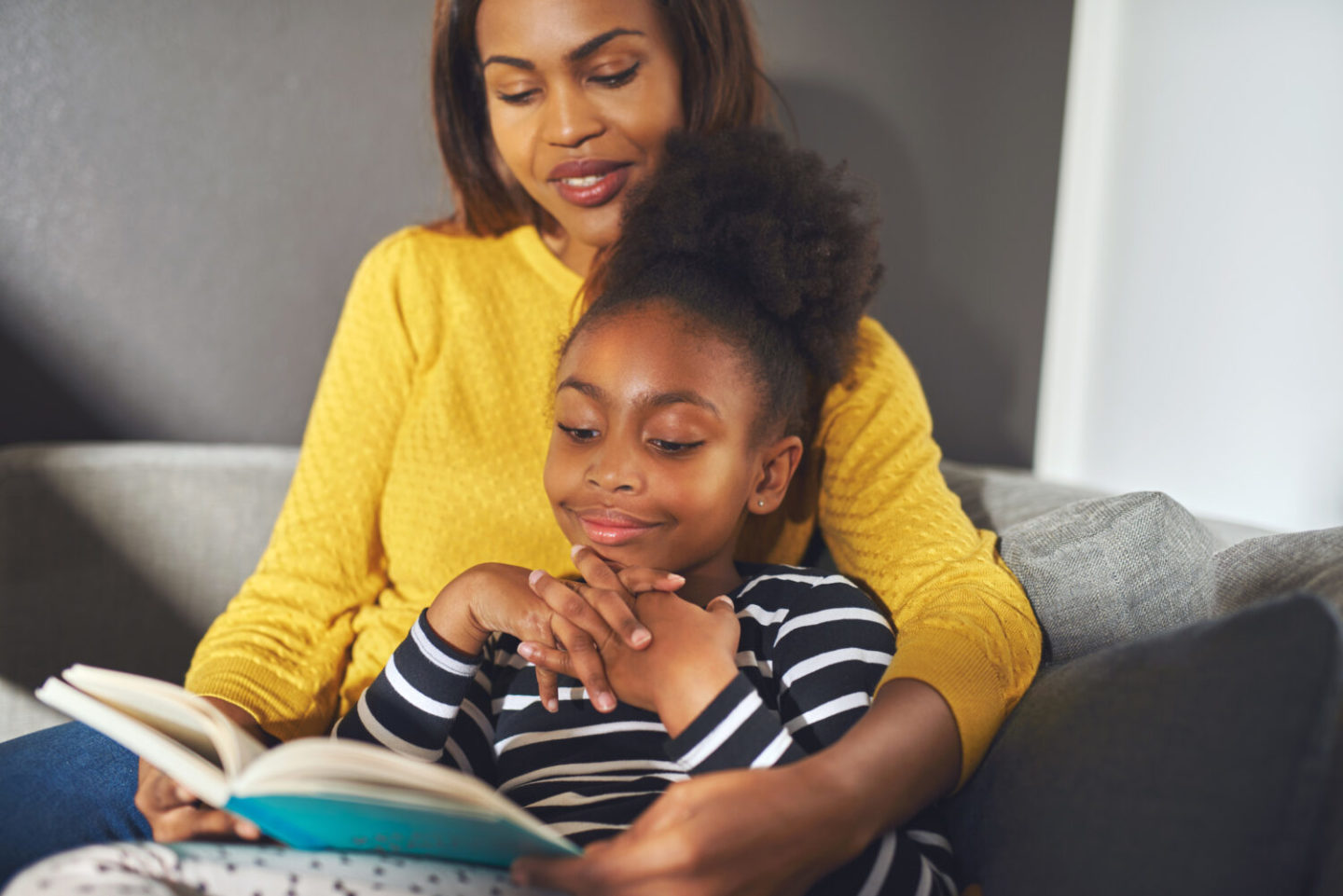 Фото мама с дочкой читают книгу. Mother Rand Doughter sitting on Sofa smiling.